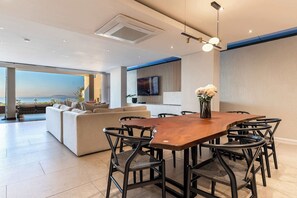 A modern dining area with a wooden table and black chairs, a sofa, and a TV on the wall. - Sea Views, Luxurious, Pool -Iconic View Green Point (Cape Town)