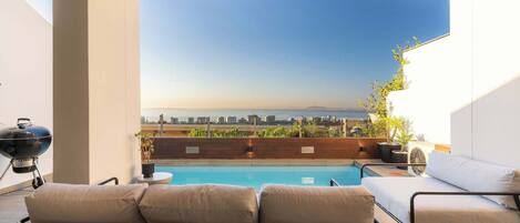 Un área de piscina en la azotea con vistas al horizonte de la ciudad, una parrilla y asientos exteriores.
