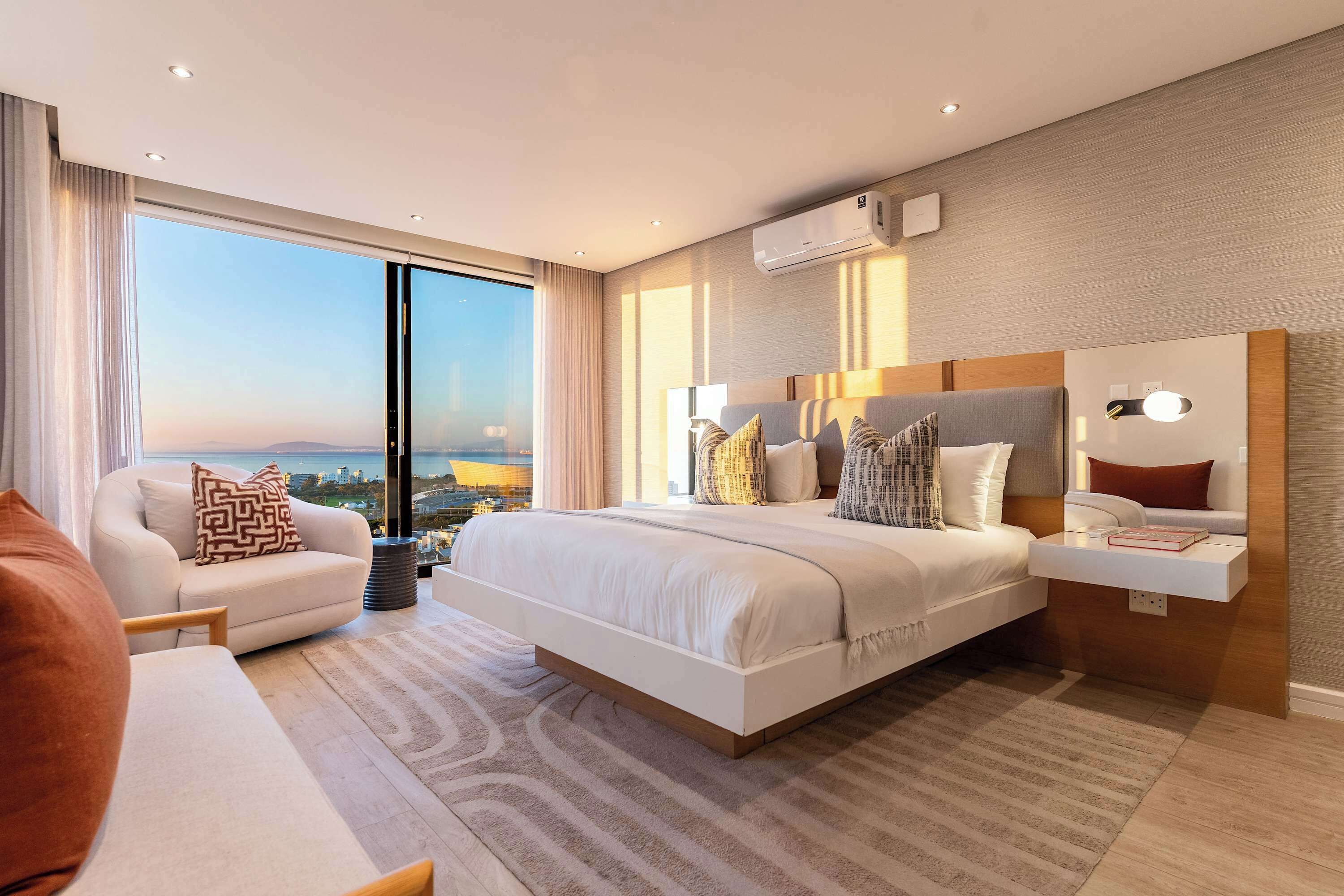 A modern hotel room with a large bed, a sofa, a bedside table, and a view of the city.