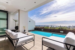 A rooftop pool area with two lounge chairs, a small table, and a potted plant. - Sea Views, Luxurious, Pool -Iconic View Green Point (Cape Town)