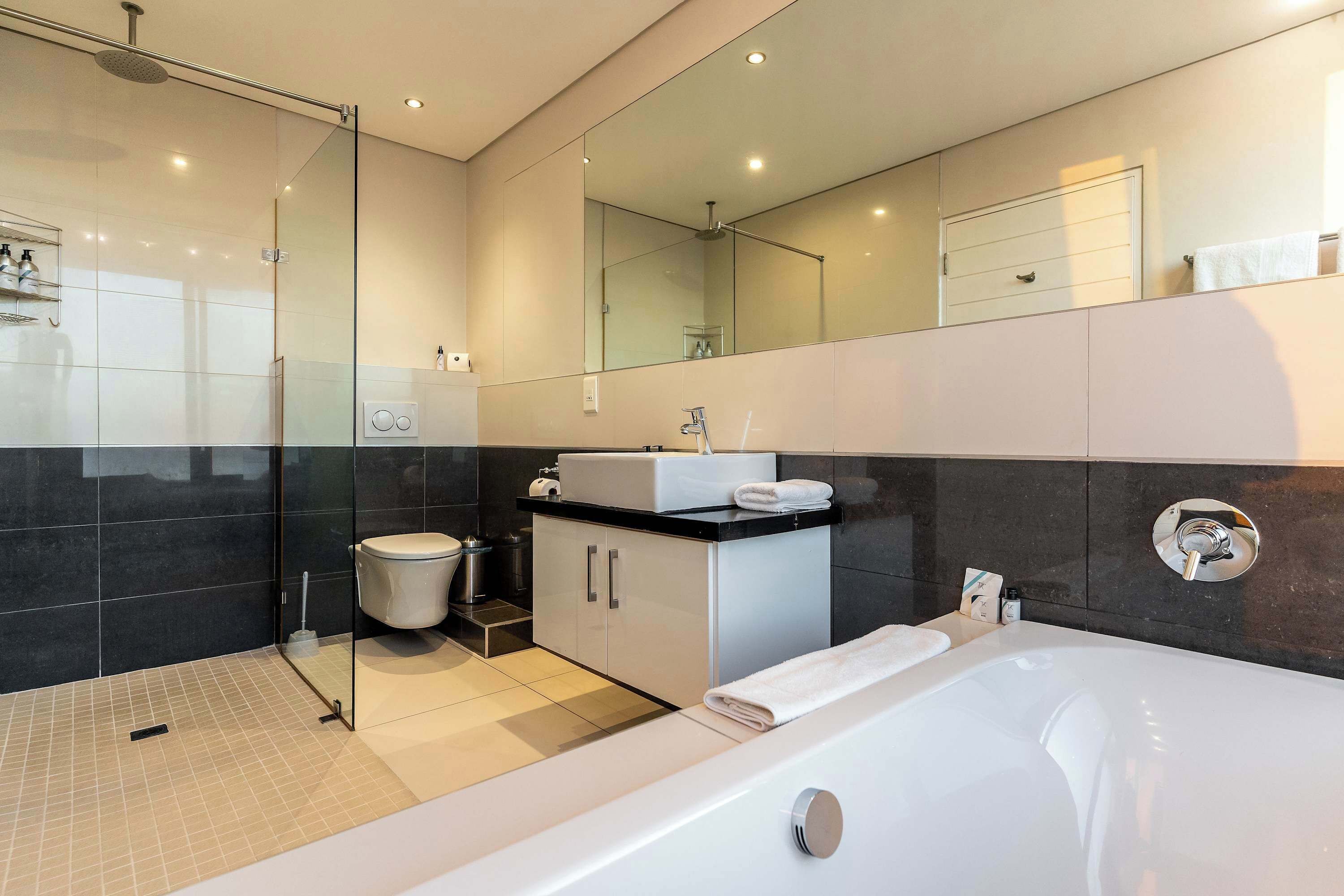 Een moderne badkamer met een douche met glazen wand, een bad, een toilet en een wastafel met spiegel.