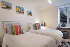 Een slaapkamer met twee bedden, witte beddengoed, kleurrijke kussens en kunst aan de muren.