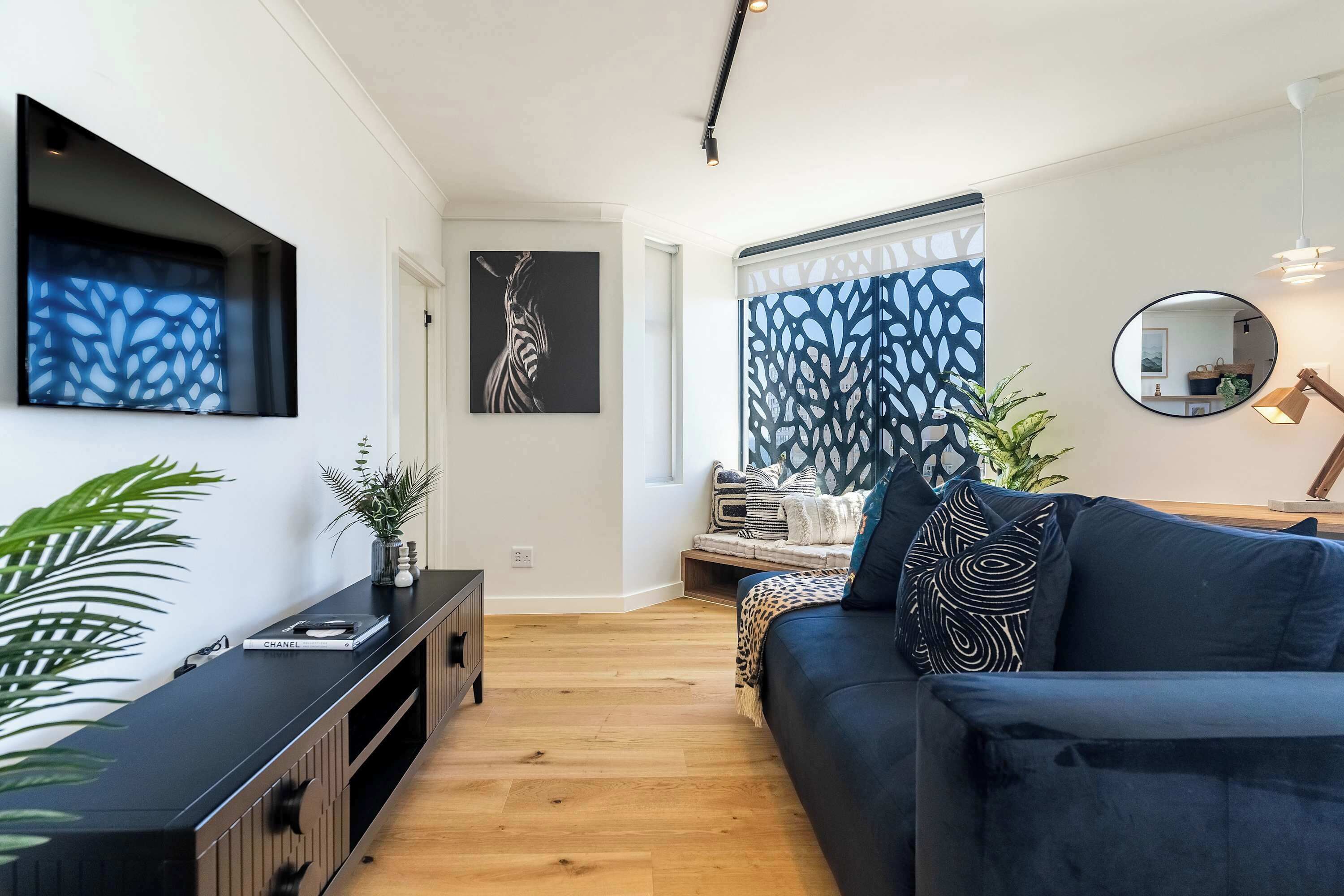Een moderne woonkamer met een donkerblauwe bank, een zwarte tv-meubel en een groot abstract schilderij aan de muur.