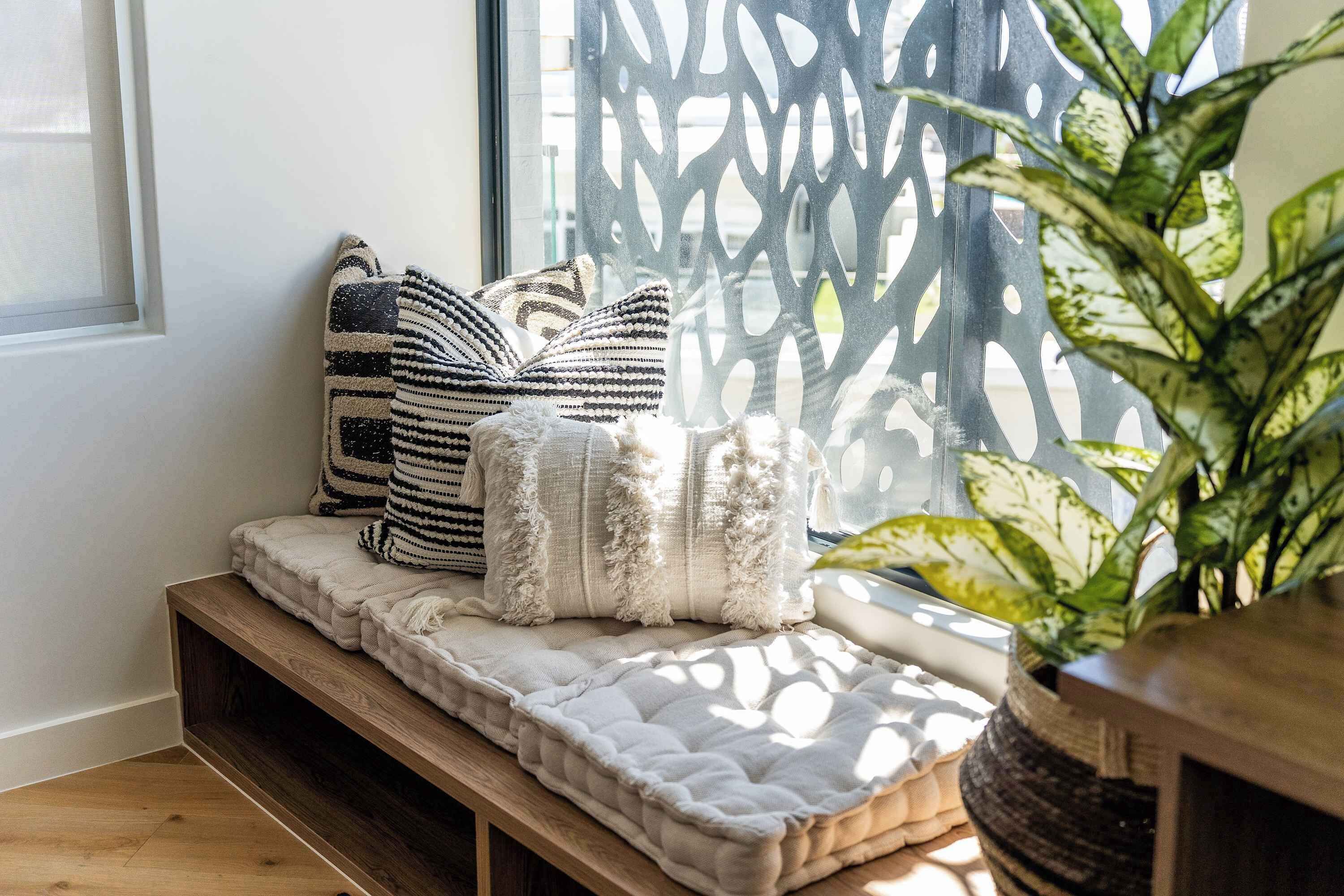 A cozy seating area with a cushioned bench, patterned pillows, and a potted plant.