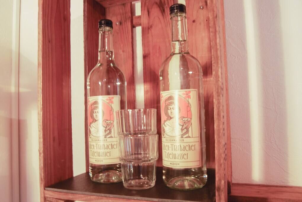 Deux bouteilles de « Helle-Träbacher », une liqueur moyennement alcoolisée, et un petit verre posés sur une étagère en bois.