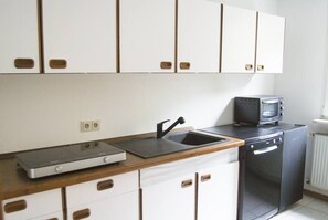 Una cuina compacta amb armaris blancs, un rentaplats negre i un microones al taulell.