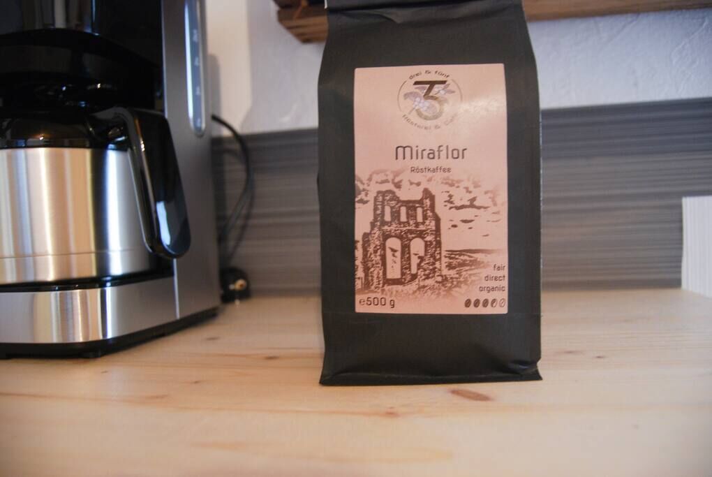 Eine Packung Kaffee mit dem Aufdruck 'Miraflor' und einem Gewicht von 500g, platziert auf einer Holzoberfläche neben einem Edelstahlgerät.