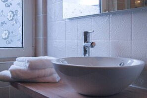 Ein Badezimmer mit einem großzügigen Vessel-Waschbecken, einem Spiegel und einem Fenster mit floralem Rollo.