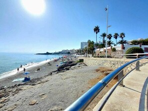 A beach with a stone wall, palm trees, and a clear sky.