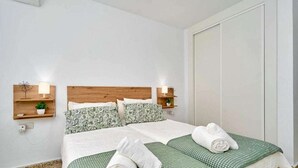 A hotel room with a wooden headboard, two beds with green and white bedding, two bedside tables with lamps, and a white door. - Nerja Beachfront Apartment Sea Views and Balcony (Torrijos)