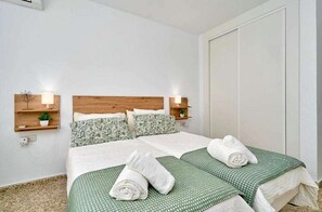 Ein Hotelzimmer mit einem hölzernen Kopfende, zwei Betten mit grün-weiß gestreifter Bettwäsche, zwei Nachttischen mit Lampen und einer weißen Tür.