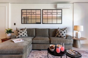 A modern living room with a sectional sofa, a coffee table with drinks, and a side table with a lamp. - 270 Views, Modern, Bo-Kaap -Table Mountain Majesty Apt (Cape Town)