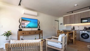 Una sala de estar moderna con televisor, muebles de mimbre y una cocina con armarios de madera y lavadora.