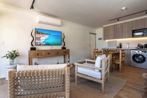 A modern living room with a television, wicker furniture, and a kitchen area with wooden cabinets and a washing machine. - Mountain Views, Shared Gym, CPT - York Urban Studio (Cape Town)