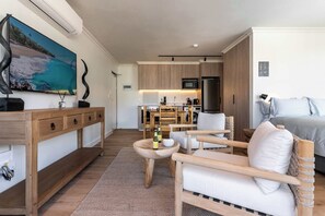 A modern hotel room with a wooden console table, a seating area with a sofa and chairs, a kitchen area with a microwave and refrigerator, and a large TV mounted on the wall. - Mountain Views, Shared Gym, CPT - York Urban Studio (Cape Town)