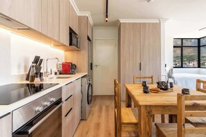 A modern kitchen with wooden cabinets, stainless steel appliances, and a dining area with a wooden table and chairs. - Mountain Views, Shared Gym, CPT - York Urban Studio (Cape Town)