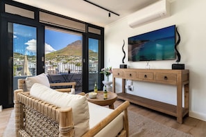 A balcony with a view of a city and a mountain, furnished with a sofa, a table with bottles, and a console table with a painting. - Mountain Views, Shared Gym, CPT - York Urban Studio (Cape Town)