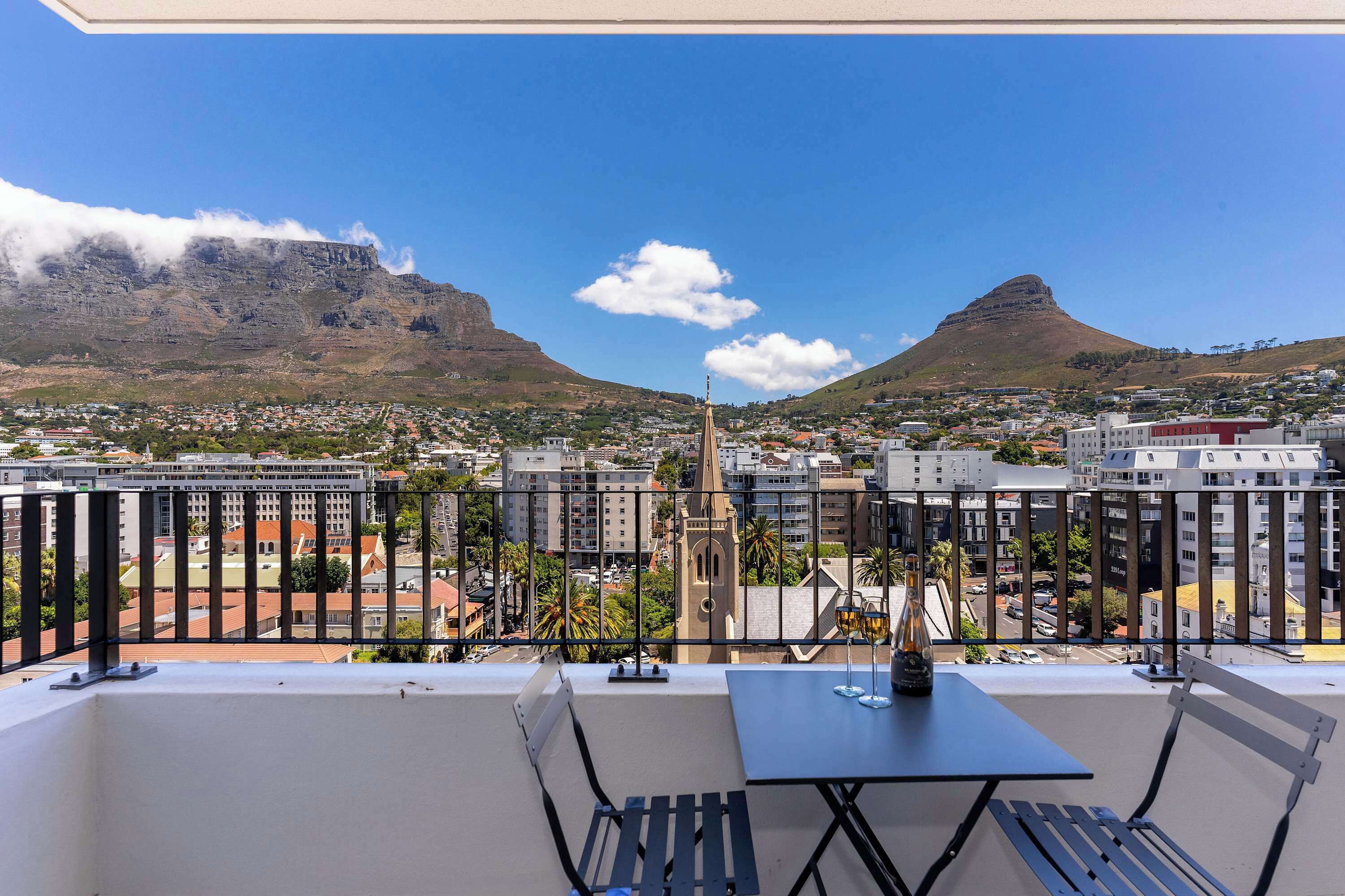 Un balcon avec une table et des chaises donnant sur un paysage urbain, avec des montagnes et des bâtiments en toile de fond.