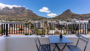 Un balcón con mesa y sillas que ofrece vistas de un paisaje urbano con montañas y edificios.