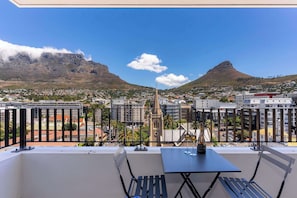 A balcony with a table and chairs overlooking a cityscape with mountains and buildings. - Mountain Views, Shared Gym, CPT - York Urban Studio (Cape Town)