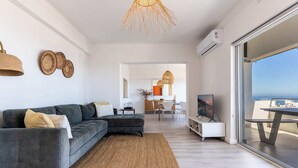 A modern living room with a grey sectional sofa, a woven rug, and a large window offering a view. - Perfect Location, Views - Bantry Bay Pearl Apt (Cape Town)