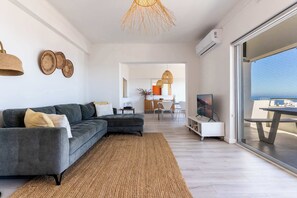 Ein modernes Wohnzimmer mit einem grauen Ecksofa, einem gewebten Teppich und einem großen Fenster mit Blick.