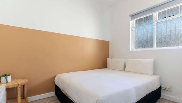 A bedroom with a bed, a small round wooden table, a white wall, and a window with a patterned blind. - Perfect Location, Views - Bantry Bay Pearl Apt (Cape Town)