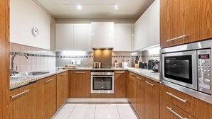 A modern kitchen with wooden cabinets, stainless steel appliances, and a tiled backsplash. - Location, View, Pool, Green Point - Royale 203 Apt (Cape Town)