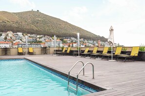 Ein Swimmingpool mit Liegestühlen und Blick auf eine Hügelstadt.