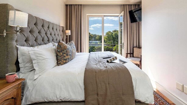 A hotel room with a large bed, a flat-screen TV mounted on the wall, and a view of the outdoors through a large window. - Location, View, Pool, Green Point - Royale 203 Apt (Cape Town)