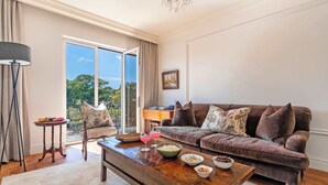 A living room with a brown sofa, a wooden coffee table, and a glass door leading to a balcony. - Location, View, Pool, Green Point - Royale 203 Apt (Cape Town)
