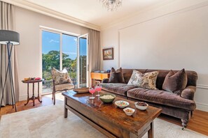Ein Wohnzimmer mit einem braunen Sofa, einem Holztisch und einer Glastür, die auf einen Balkon führt.