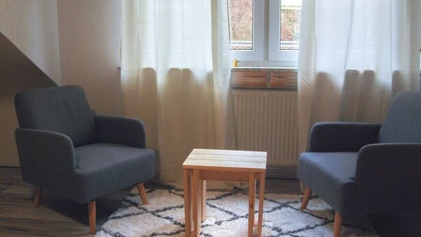 Et værelse med to mørke lænestole, et lille træbord og en tæppe med et mønster.