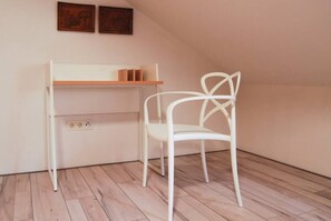 Una cadira blanca al costat d'un taulell blanc amb una prestatgeria, en una habitació amb terres de fusta i sostre inclinat.