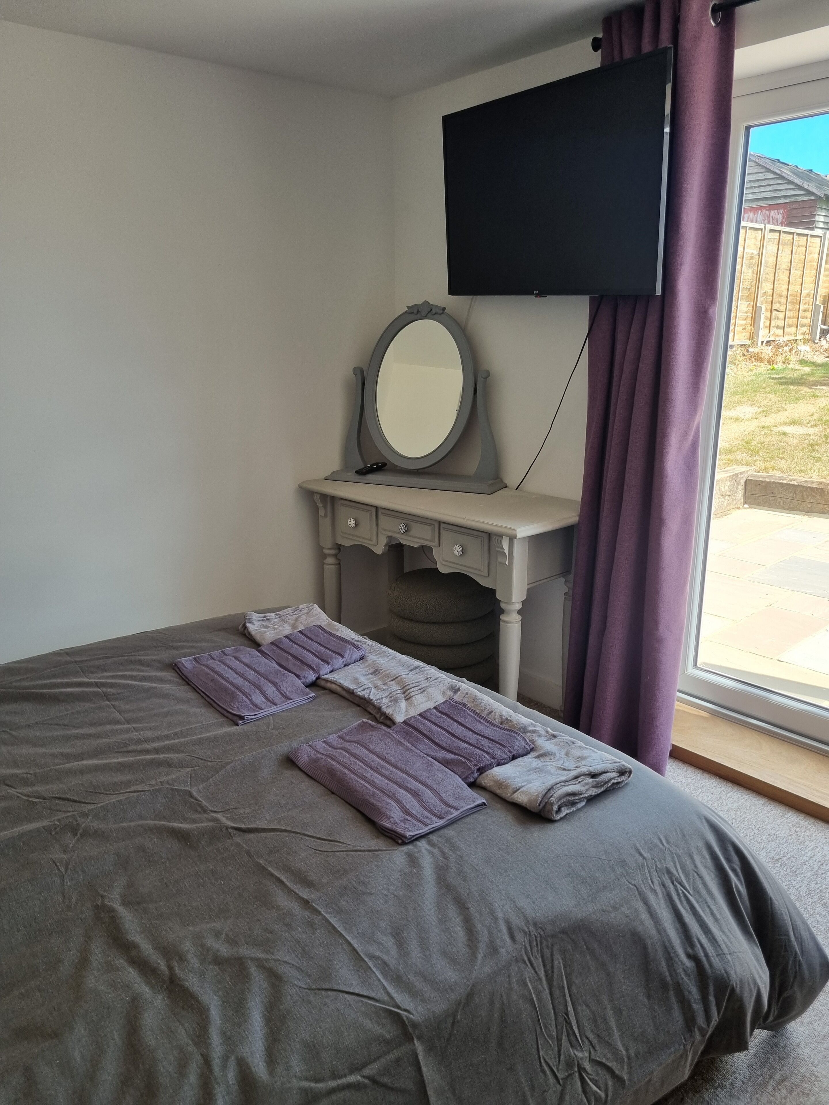 Quarto com cama, penteadeira com espelho e televisão na parede.