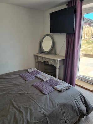A bedroom with a bed, a vanity with a mirror, and a television mounted on the wall. - Home-from-home new-build bungalow in the heart of the Isle of Wight (Ryde)
