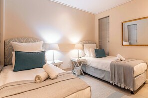 Ein Hotelzimmer mit zwei Betten, einem Nachttisch mit Lampen, einem Spiegel und einem Fenster mit Jalousien.
