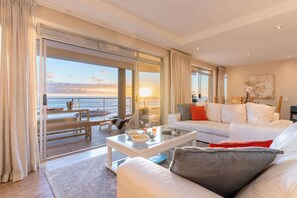 Ein geräumiger Wohnbereich mit einem großen Glasfenster, das auf einen Balkon führt, einem weißen Sofa, einem Couchtisch und einem Bild an der Wand.