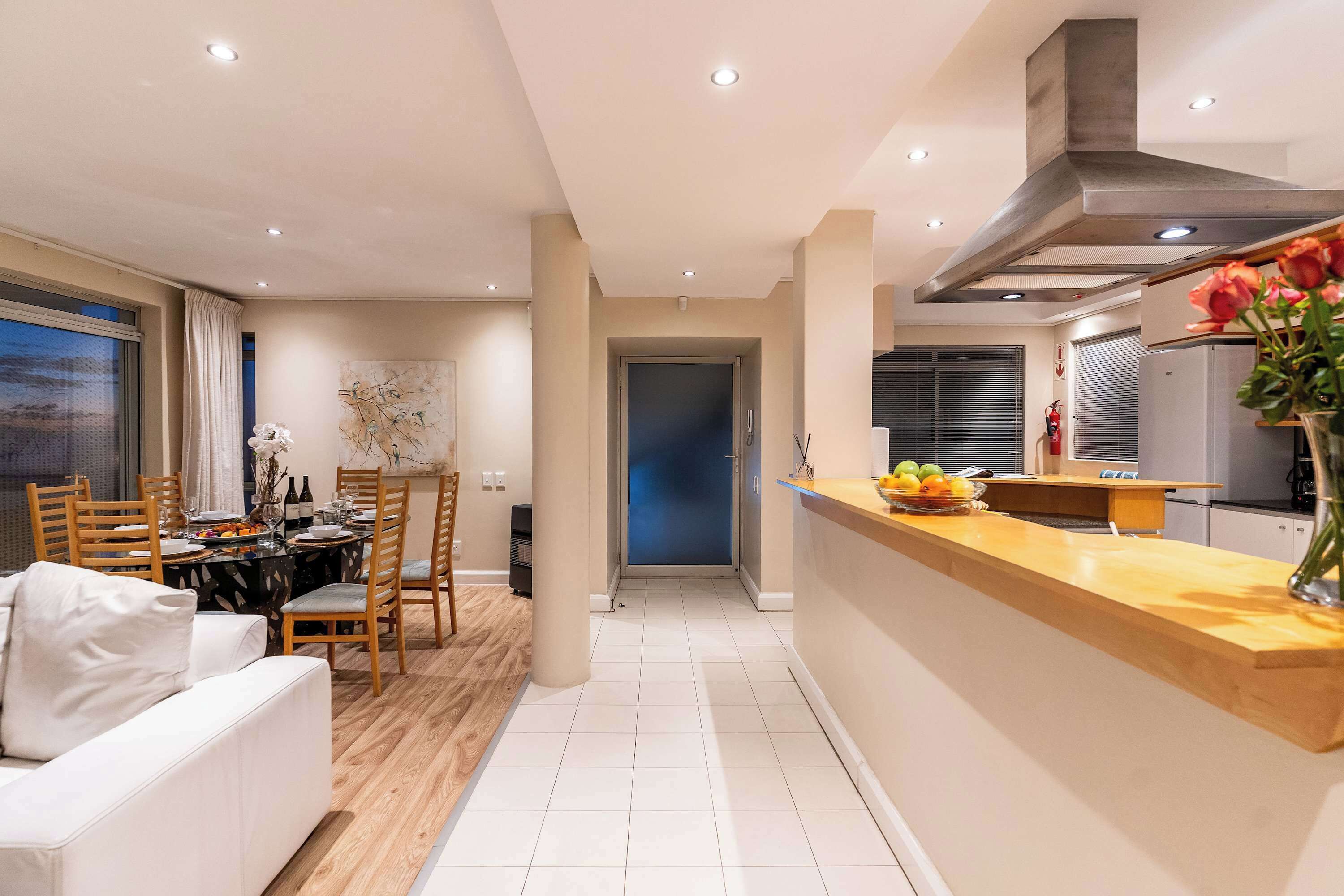 A modern kitchen with a wooden countertop, a dining area with a table set for four, and a living room with a sofa.