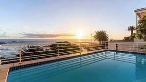 A pool with a view of the ocean at sunset. - Sunset Azure Apt - Panoramic Views, 2 min to beach (Cape Town)