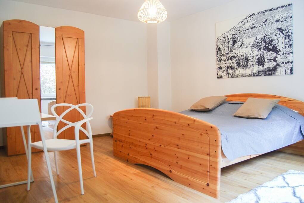 Un dormitorio con una cama de madera, una silla blanca, un escritorio y un cuadro grande en la pared.