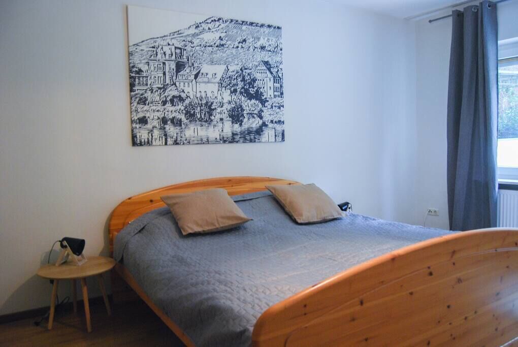 A bedroom with a wooden bed, a small bedside table, a wall-mounted artwork, and a window with curtains.