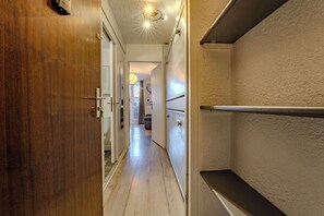 A narrow hallway with wooden flooring, a white wall with a textured finish, and a door on the left. - Slopeside Apt w/ Balcony & Views (Les Belleville)