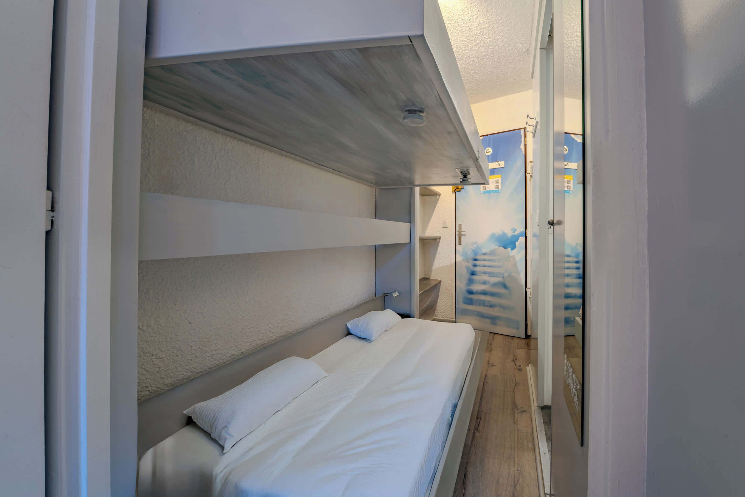 A bedroom with a bunk bed, a small bedside table, and a wall-mounted shelf.