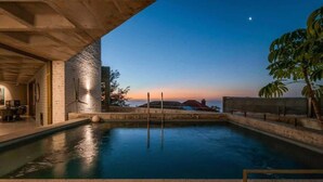 En pool med utsikt över solnedgången, en byggnad i betong och en krukväxt.