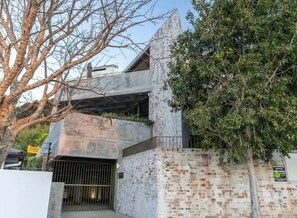 A modern building with a concrete facade, a gated entrance, and a tree in the foreground. - Luxurious Apt, Pool, Views, Sea Point - Luna Loft (Cape Town)