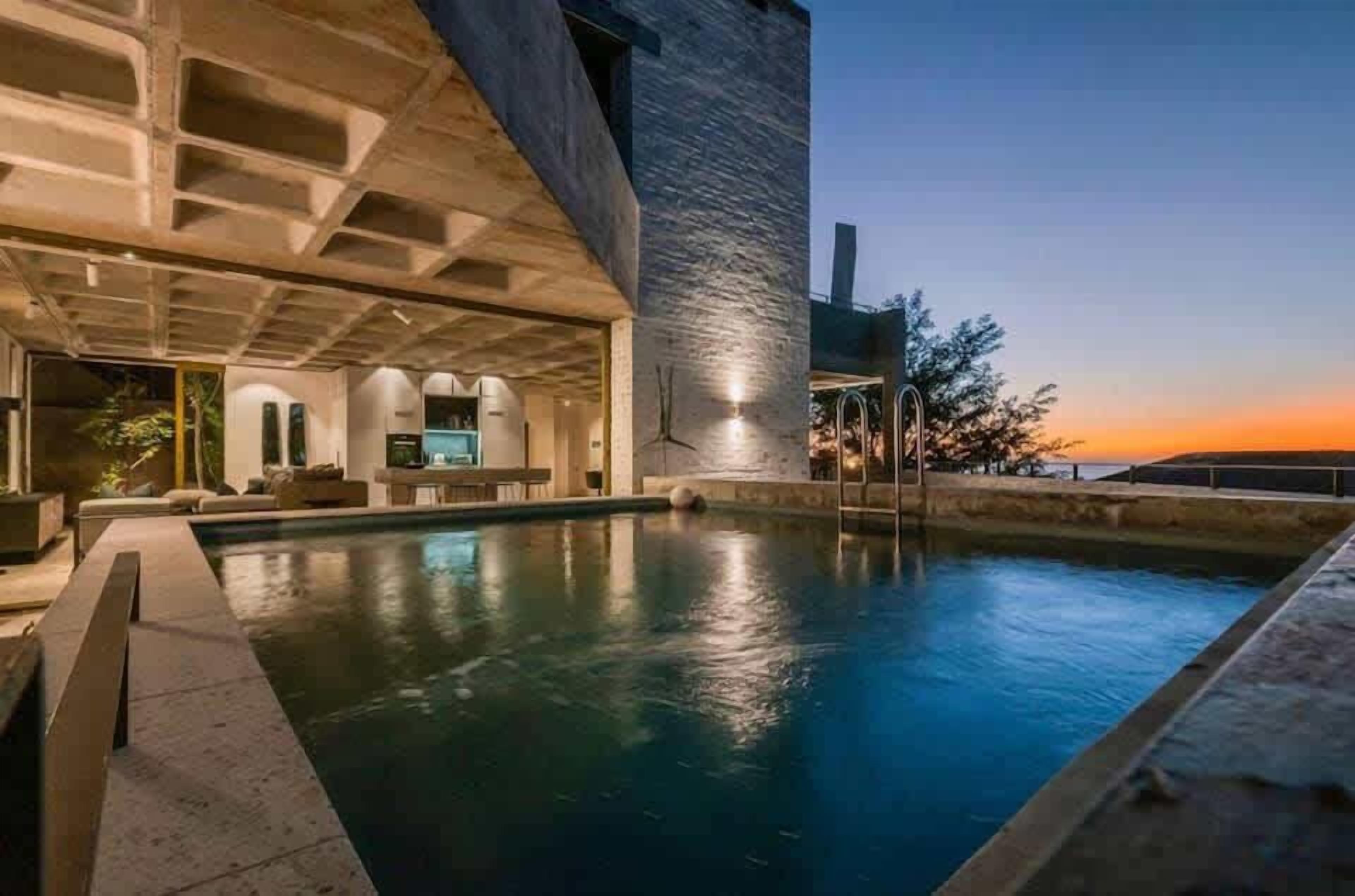 Piscina com design arquitetônico moderno, área de estar coberta e vista para o pôr do sol.