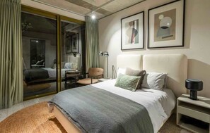 A modern bedroom with a large bed, a desk, and a chair. There are two framed artworks on the wall and a floor lamp on the nightstand. - Luxurious Apt, Pool, Views, Sea Point - Luna Loft (Cape Town)