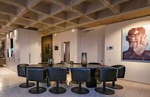 Ein moderner Konferenzraum mit einem runden Tisch und acht Stühlen, einem großen, abstrakten Gemälde an der Wand und einer Tür, die in einen anderen Raum führt.