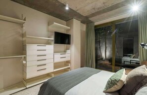 Ein modernes Schlafzimmer mit einem Bett, einem an der Wand montierten Fernseher und einer Schiebeglastür, die zu einem Außenbereich führt.